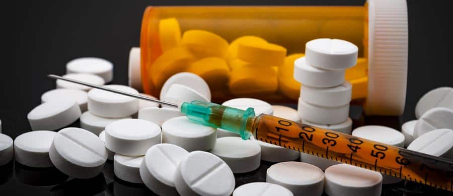 What Other Factors Increase the Risk of Addiction? drug pills and a syringe on a table